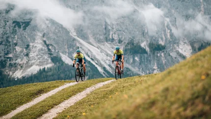 Zwei Radfahrer fahren auf einem Bergweg vor nebligen Alpenfelsen