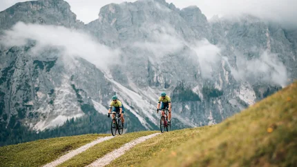 Zwei Radfahrer fahren auf einem Bergweg vor nebligen Alpenfelsen