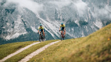 Zwei Radfahrer fahren auf einem Bergweg vor nebligen Alpenfelsen