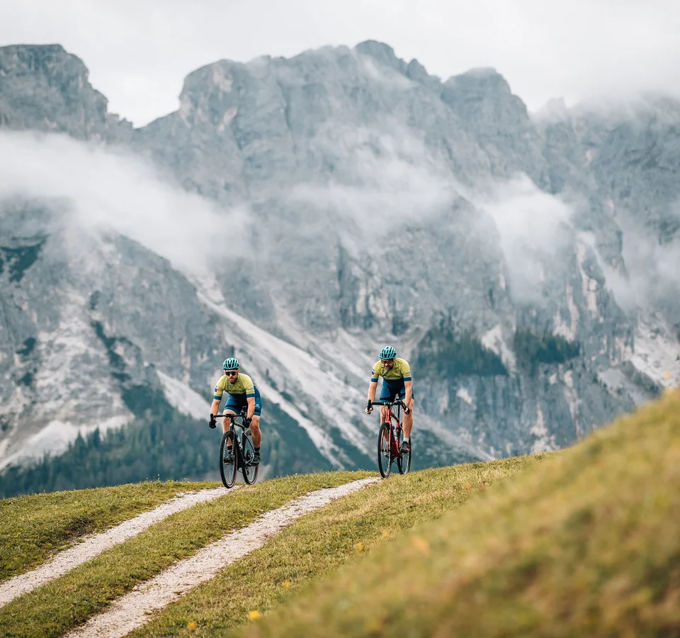 Zwei Radfahrer fahren auf einem Bergweg vor nebligen Alpenfelsen