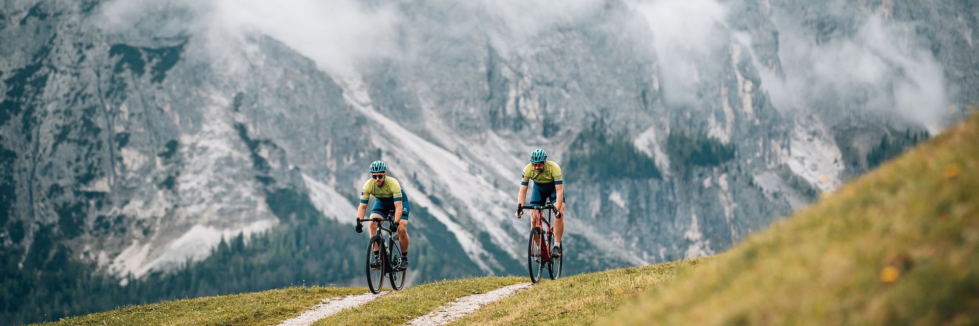 Zwei Radfahrer fahren auf einem Bergweg vor nebligen Alpenfelsen