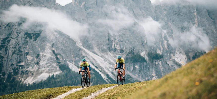 Zwei Radfahrer fahren auf einem Bergweg vor nebligen Alpenfelsen
