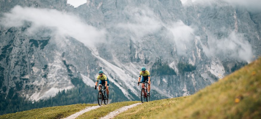 Zwei Radfahrer fahren auf einem Bergweg vor nebligen Alpenfelsen