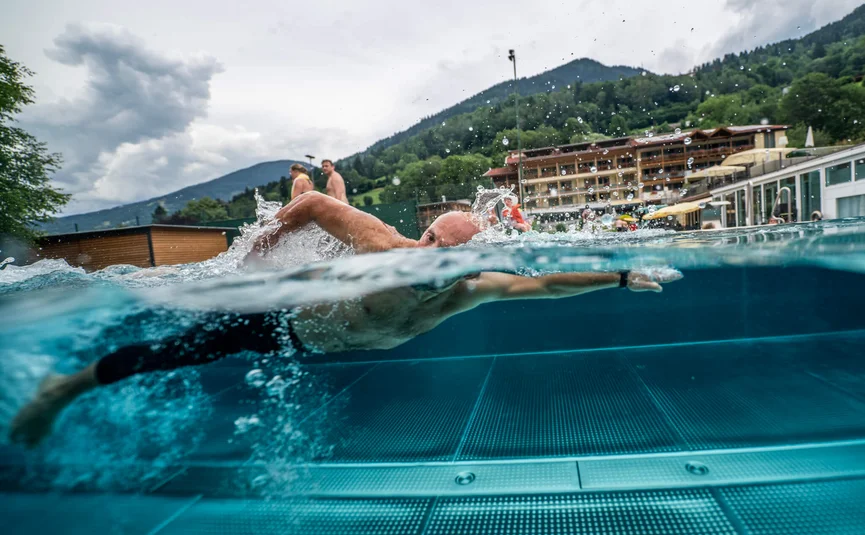 Mann schwimmt im Pool vor Bergkulisse bei bewölktem Himmel