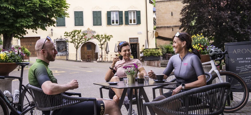 Gravel & Törggelen: Warum Tramin im Herbst perfekt für Gravelbiker ist © Heiko Mandl Drei Radfahrer sitzen im Freien und trinken Kaffee in einem Stadtzentrum