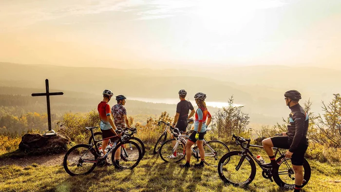 Fünf Radfahrer mit Helmen stehen auf einem Hügel mit Blick auf das Tal bei Sonnenuntergang
