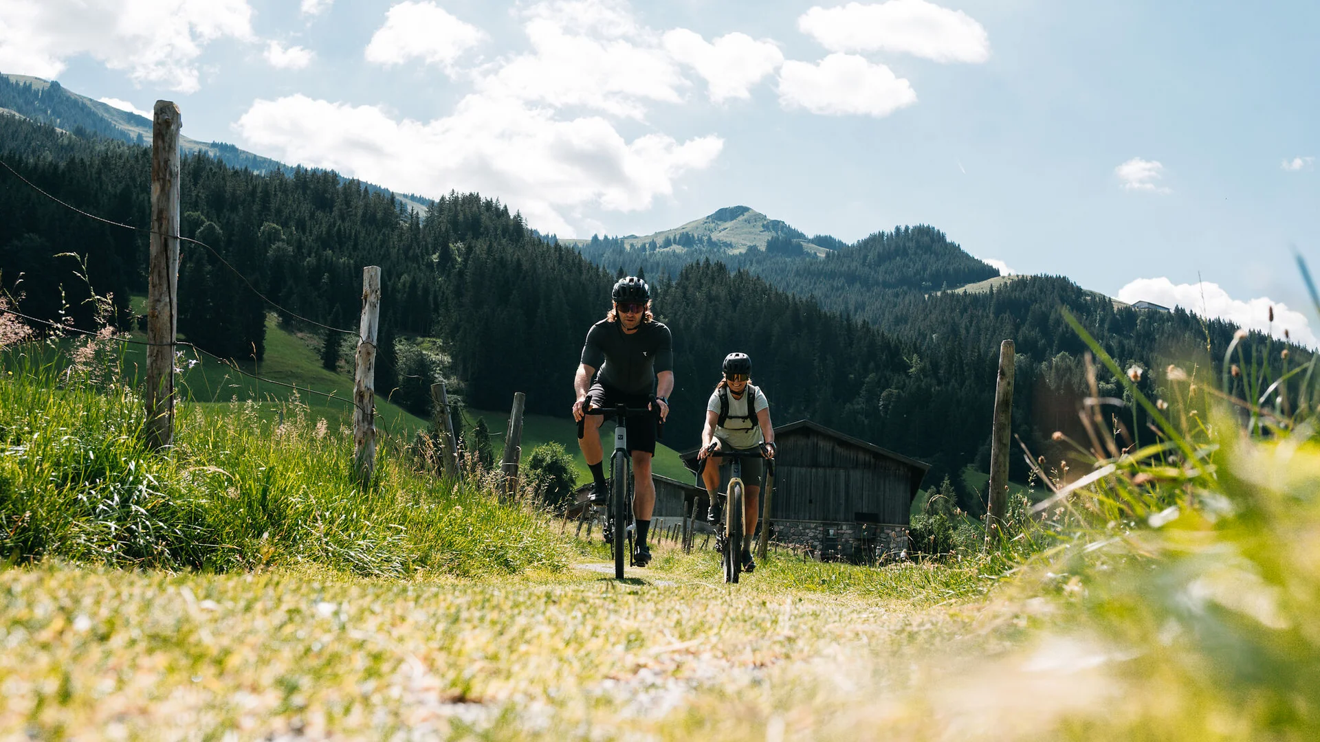 Graveln in den Kitzbüheler Alpen © Martina Wunderle / Flo Distl Zwei Radfahrer fahren auf einem Weg in den Bergen bei sonnigem Wetter