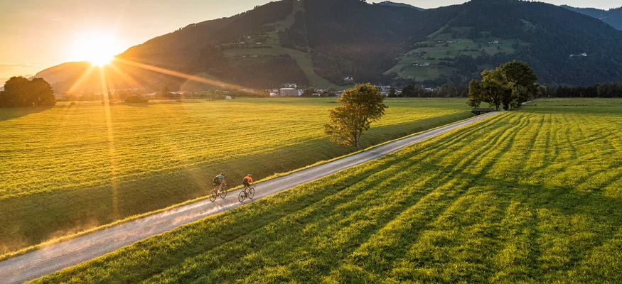 Aktivhotel Alpendorf **** © SalzburgerLand Tourismus Zwei Radfahrer auf Landweg bei Sonnenuntergang in grüner Berglandschaft