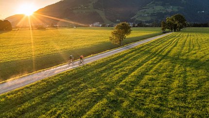 Zwei Radfahrer auf Landweg bei Sonnenuntergang in grüner Berglandschaft