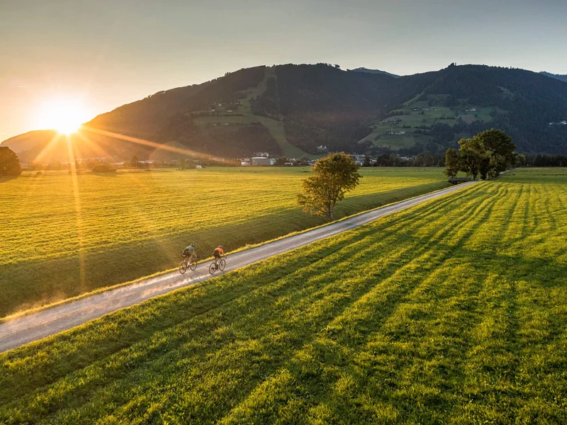 Gravelbike Holidays © SalzburgerLand Tourismus Zwei Radfahrer auf Landweg bei Sonnenuntergang in grüner Berglandschaft