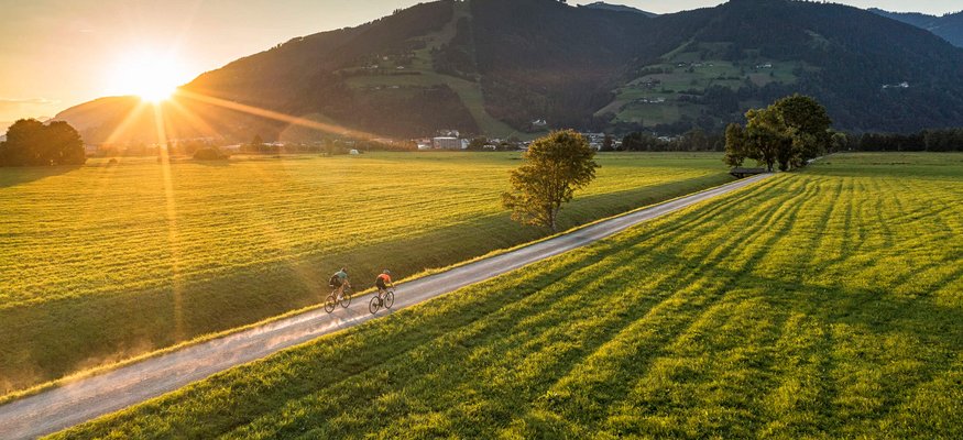 Zwei Radfahrer auf Landweg bei Sonnenuntergang in grüner Berglandschaft