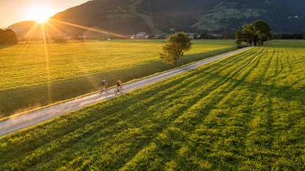 Two cyclists on rural path at sunset in green mountain landscape