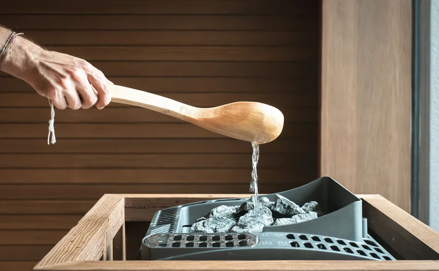 Water being poured with a wooden ladle on hot sauna stones