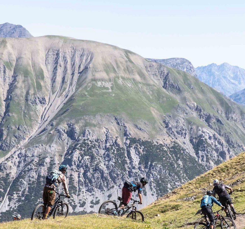 Gruppe Mountainbiker fährt auf Bergpfad mit Alpen im Hintergrund