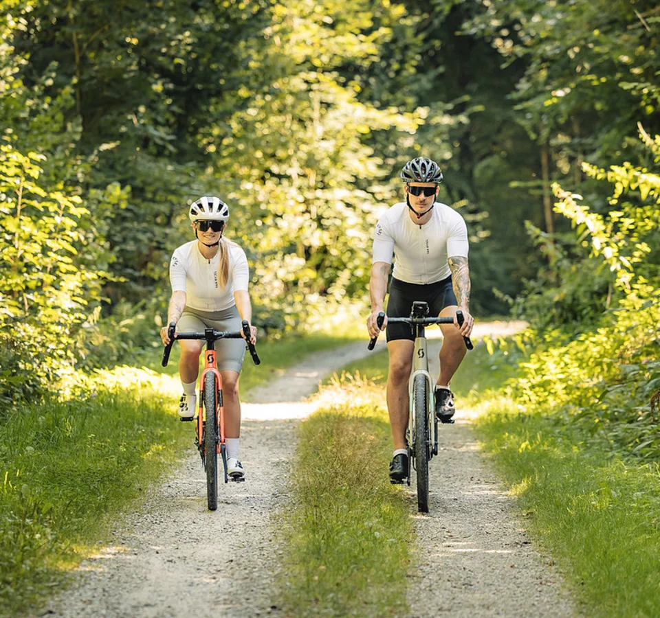 Gravelbiken im Bayerischen Wald © Stefan J. Wolf Photography Zwei Radfahrer in weißer Sportkleidung fahren auf einem Waldweg