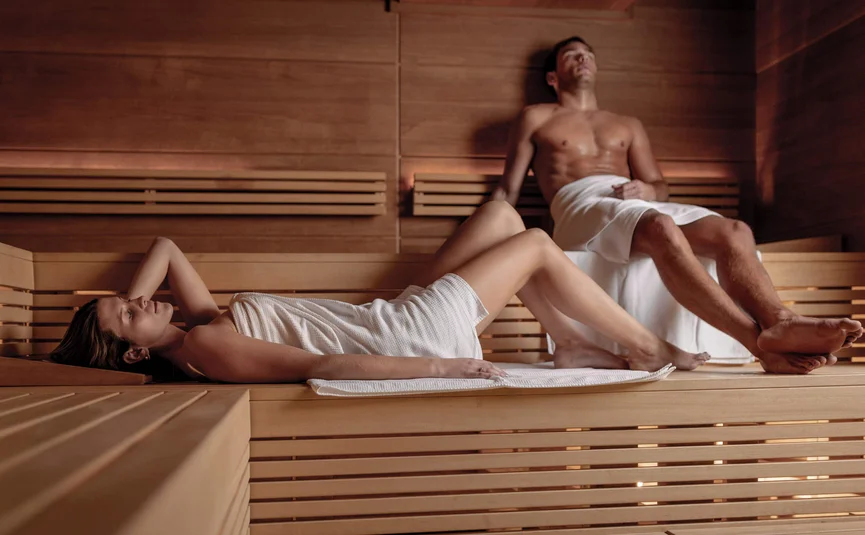 Mann und Frau entspannen in Sauna auf Holzbänken mit Handtüchern