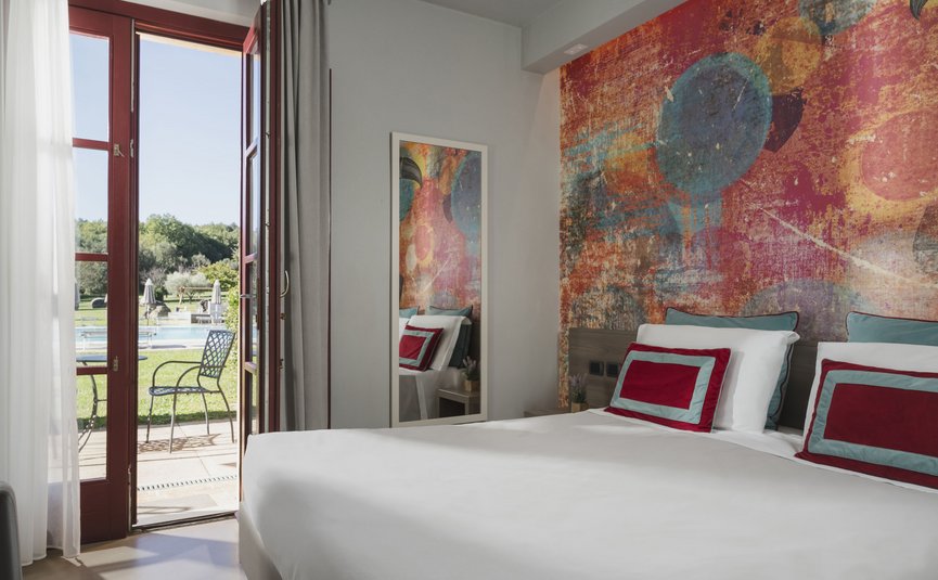 Hotel & Restaurant Casolare Le Terre Rosse ***S © Hotel Casolare Le Terre Rosse Hell eingerichtetes Schlafzimmer mit Farbwand und Blick auf Terrasse und Pool