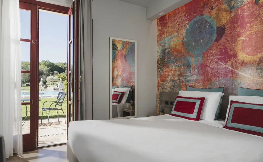 Bright hotel room with colorful wall and door opening to garden and pool