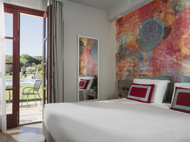 Gravelbiken in der Toskana © Hotel Casolare Le Terre Rosse Hell eingerichtetes Schlafzimmer mit Farbwand und Blick auf Terrasse und Pool