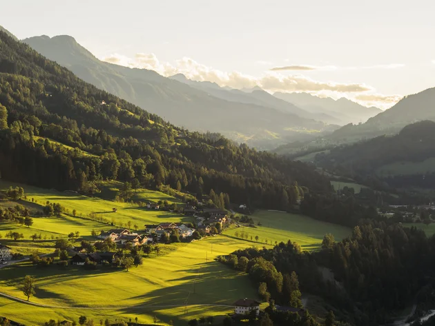 Sonniges Tal mit grünen Feldern und kleinen Häusern umgeben von Bergen