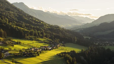 Sonniges Tal mit grünen Feldern und kleinen Häusern umgeben von Bergen