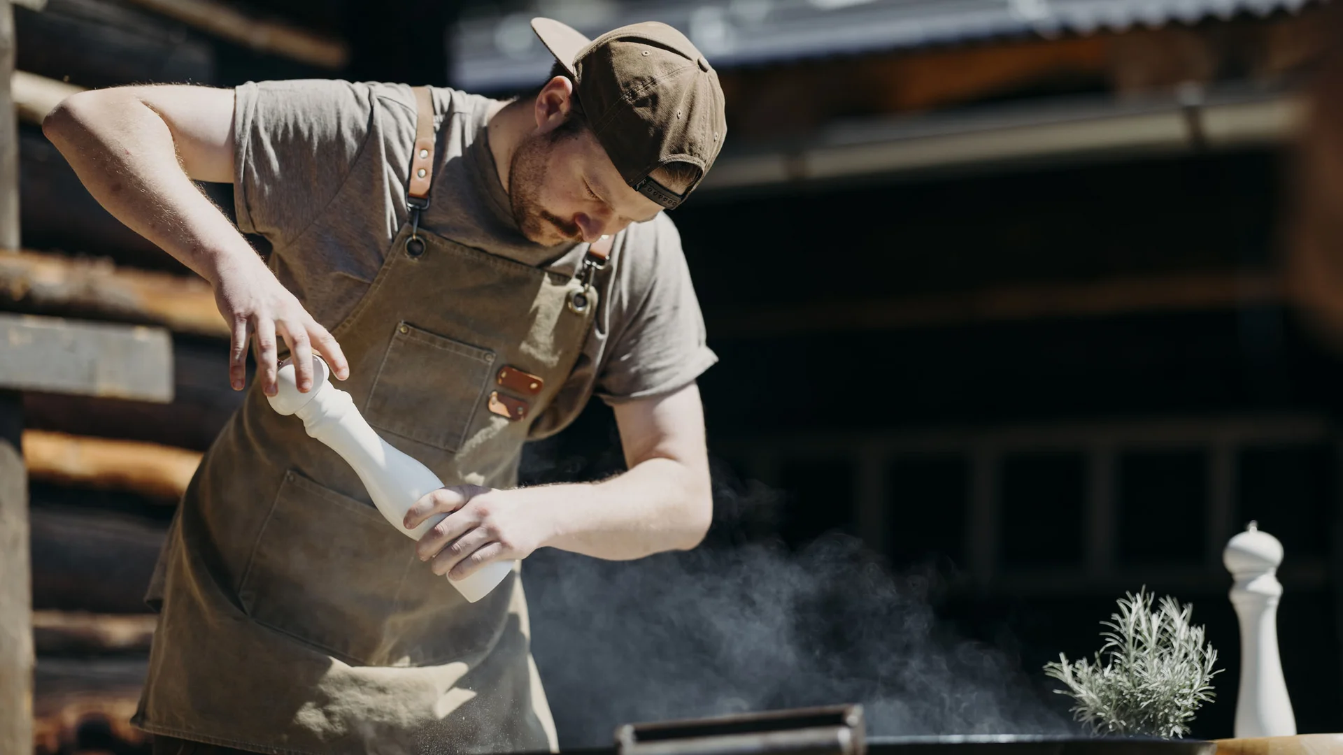 Mann in Schürze würzt Essen mit Pfeffermühle am Grill