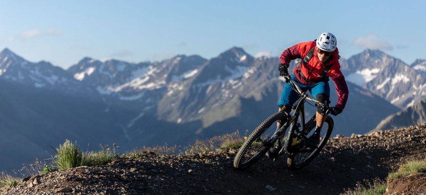 Mountainbiker fährt auf einem Gebirgspfad mit Alpen im Hintergrund