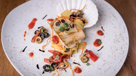 Gourmetgericht mit gebratenem Fisch, Pasta und Oliven auf weißem Teller