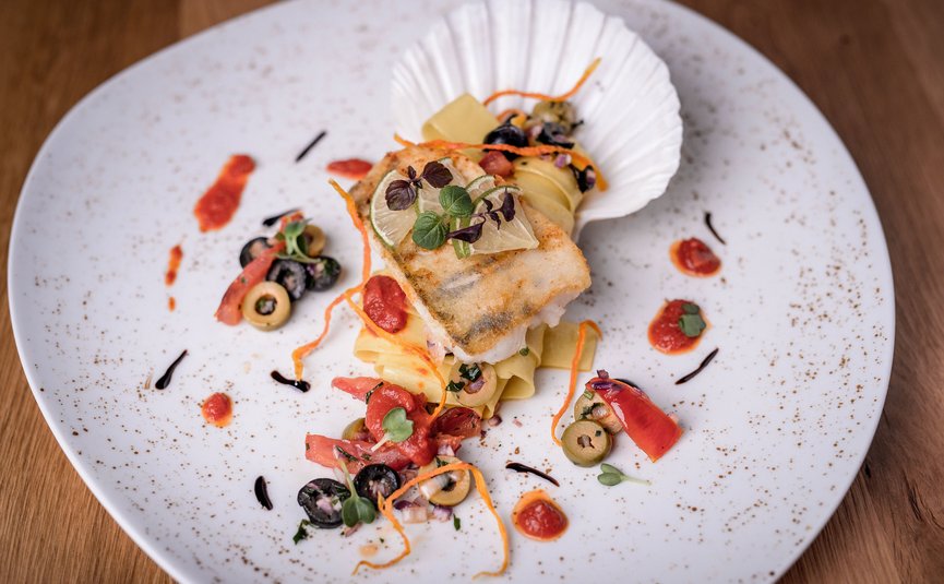 Gourmetgericht mit gebratenem Fisch, Pasta und Oliven auf weißem Teller