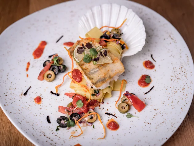 Gourmetgericht mit gebratenem Fisch, Pasta und Oliven auf weißem Teller