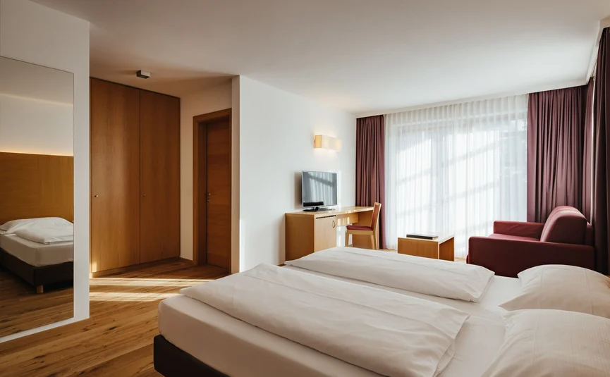 Helles Hotelzimmer mit Doppelbett, Schreibtisch, Fernseher und Sofa