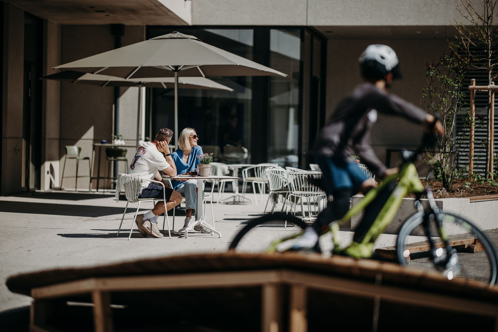 Dips&Drops - HOTEL · SPORTS · SPA · RESTAURANTS ****S © Matthias Warter Couple sitting outside at a table under umbrella, cyclist riding past