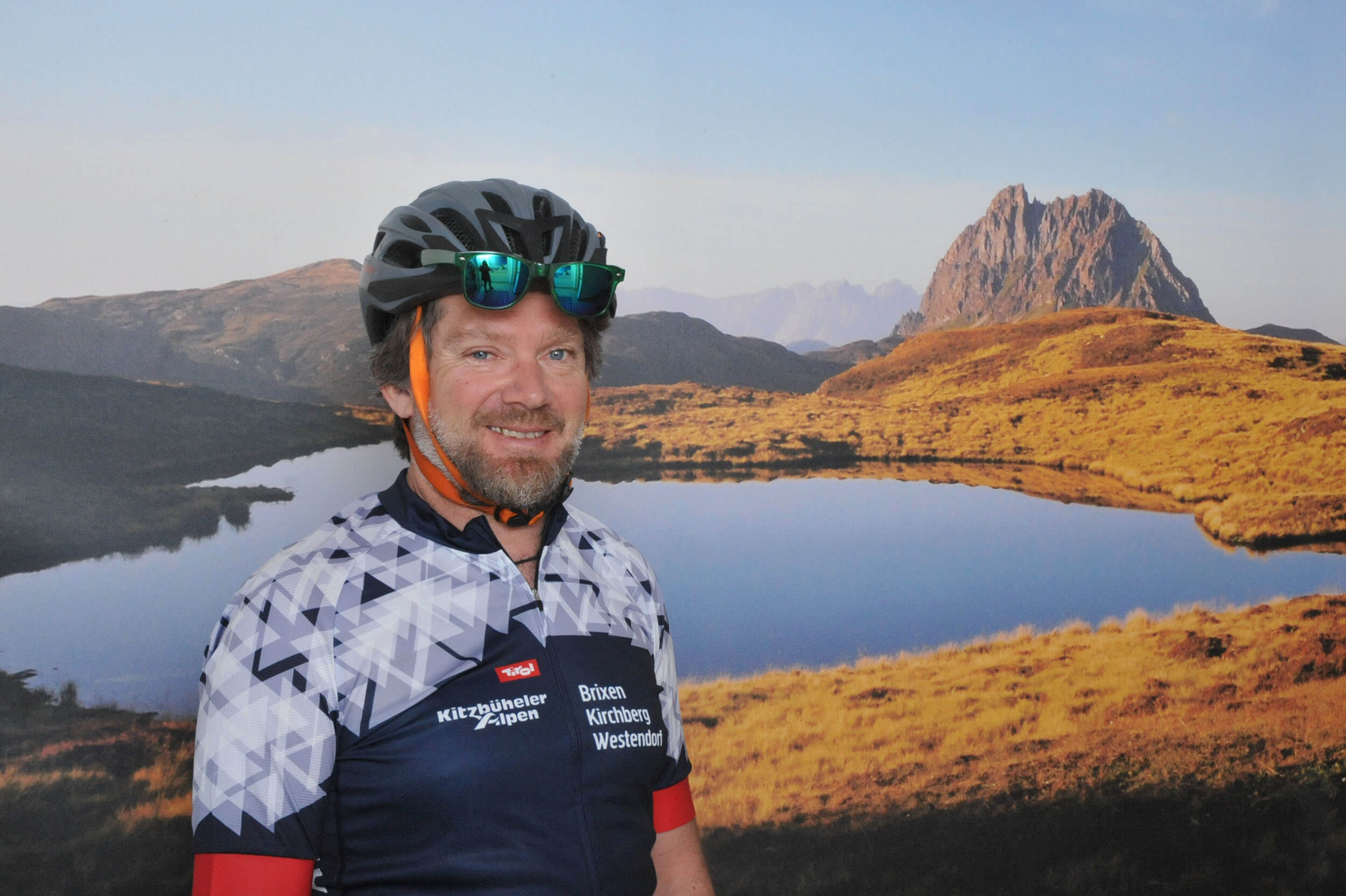 Mann mit Fahrradhelm vor Bergsee und Felsen im Hintergrund